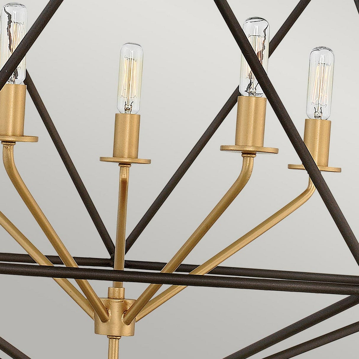 A detailed view of the Astrid 5 Light Chandelier - Matte Bronze & Gold highlights four exposed Edison-style bulbs set in gold sockets. The chandelier features a geometric outer cage design, framed by intersecting black metal rods that contribute to its modern, industrial aesthetic against a neutral backdrop.