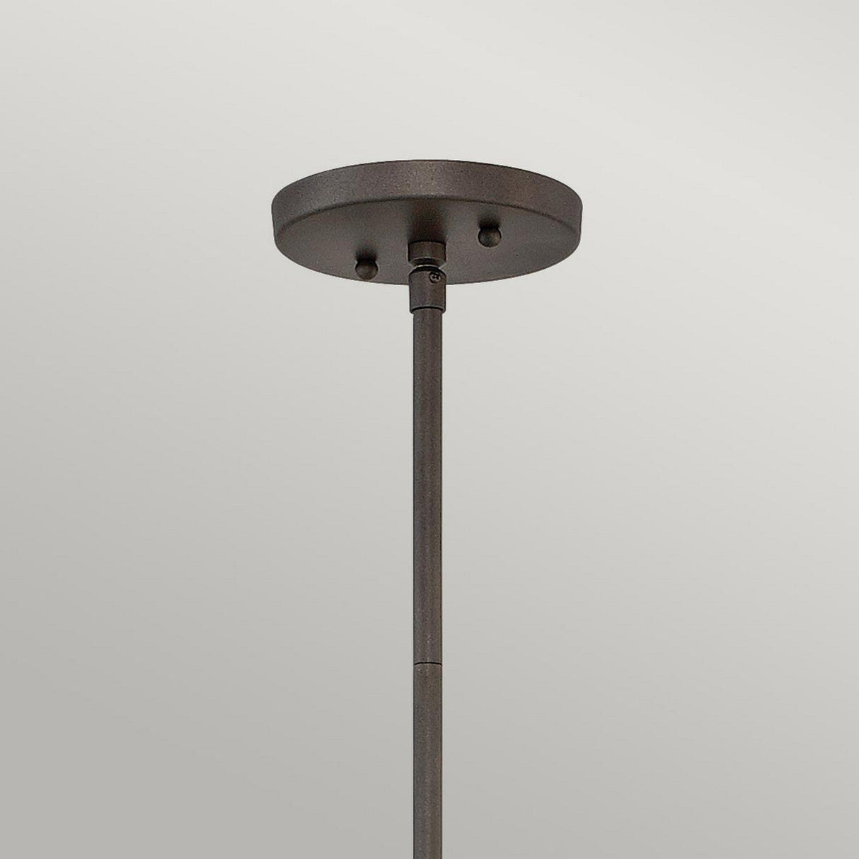 A close-up view reveals the geometric elegance of the Astrid Mini Pendant in its matte bronze and gold finish, showcasing a minimalist, industrial design. Its round base is securely attached to a plain, light-colored ceiling with a rod that extends downward.