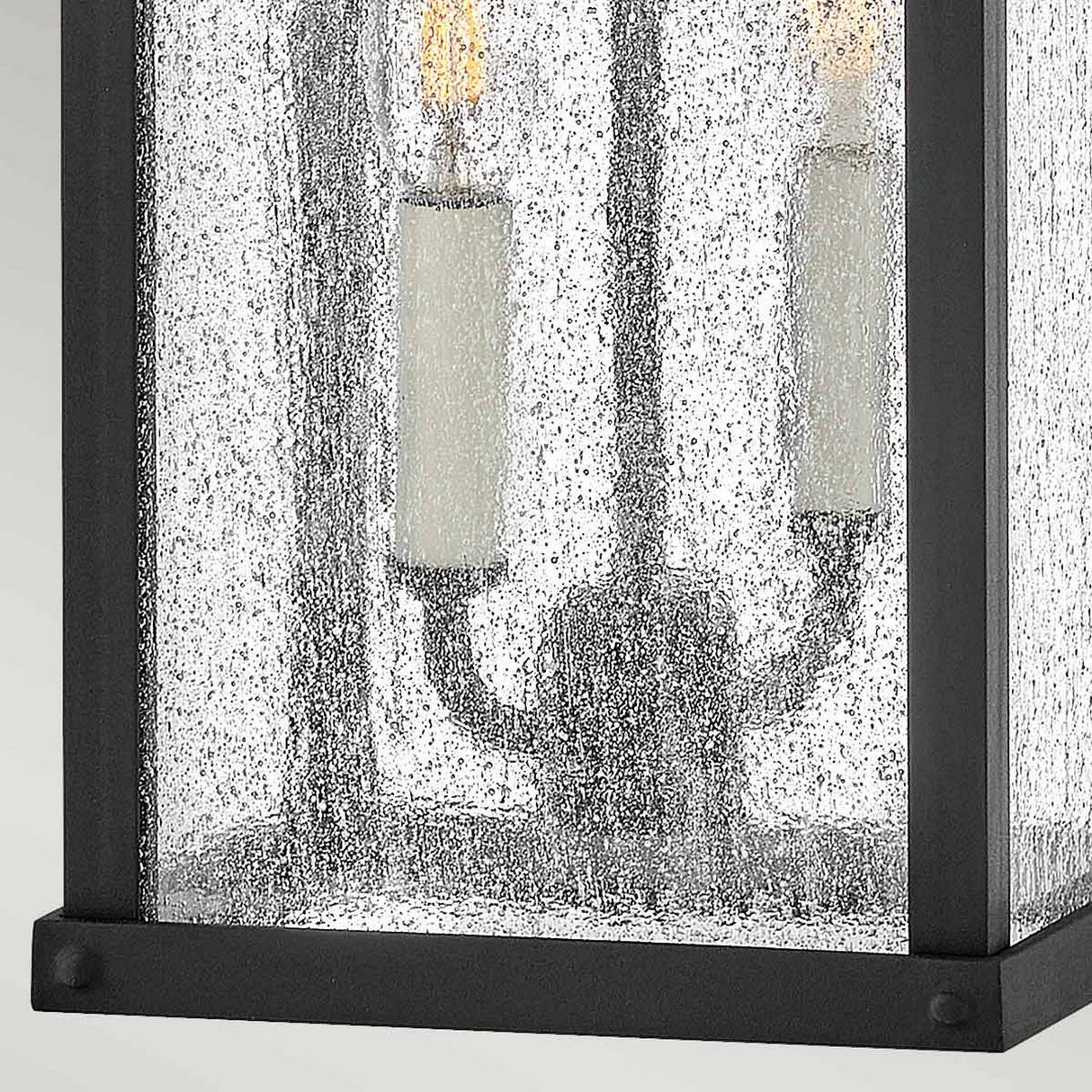 Close-up of the Beacon Hill 2 Light Outdoor Medium Wall Lantern - Black, featuring two candle-style bulbs. The glass, with its rain-soaked texture, gives this fixture a rustic and elegant design inspired by the Museum aesthetic.