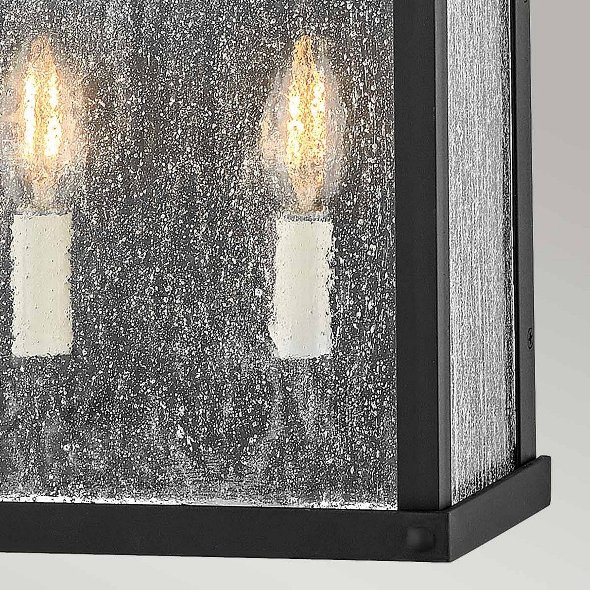 Close-up of a Beacon Hill 2 Light Outdoor Half Wall Lantern in black, featuring a museum black aluminum frame and seeded glass panel, with two candle-shaped LED bulbs that emit a warm glow.