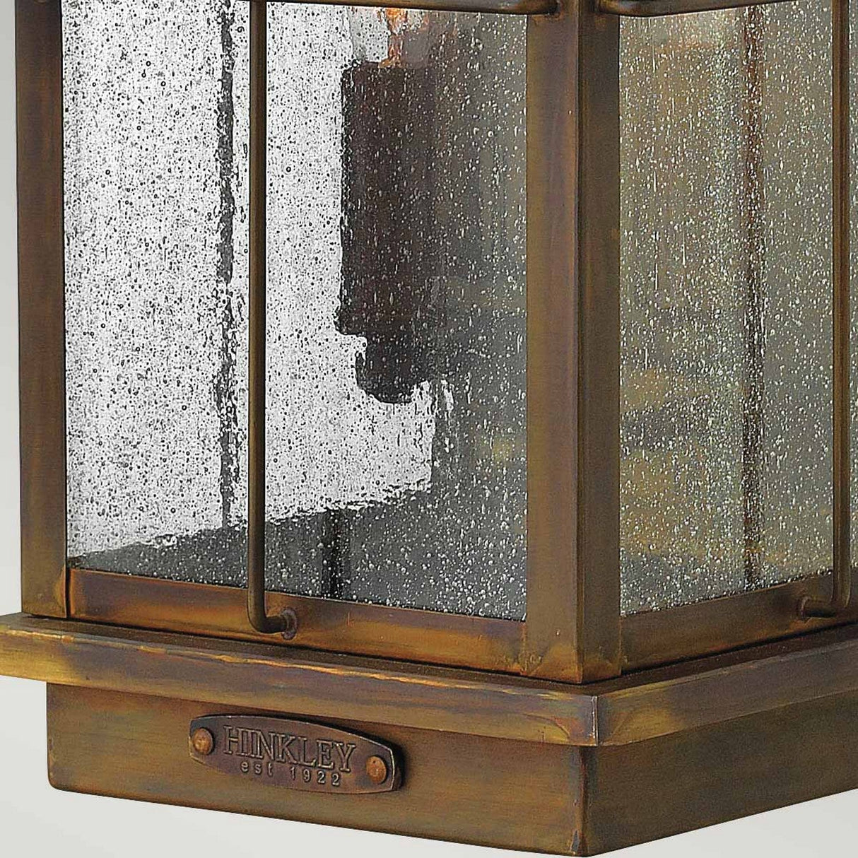 Close-up of the Bingham 3 Light Outdoor Large Wall Lantern in brown, featuring clear glass panels with raindrops on the surface. Its weathered bronze finish and vintage aesthetic are enhanced by a metal plaque at the base that reads Hinkley est 1922.