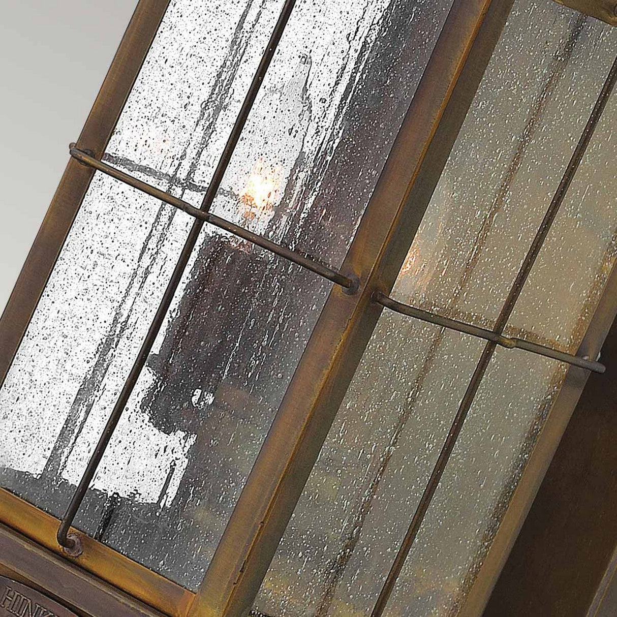 A close-up of the Bingham 3 Light Outdoor Medium Wall Lantern in brown, featuring a weathered metal frame and glass panes adorned with raindrops. The softly lit background highlights its rustic, nautical-inspired design, showcasing timeless charm.