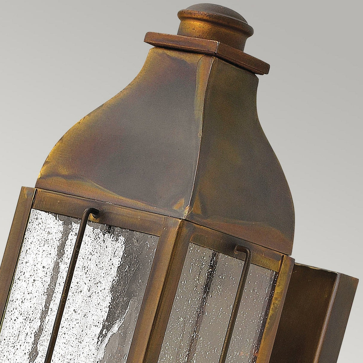 Close-up of the Bingham 1 Light Outdoor Small Wall Lantern in a rustic weathered bronze finish, showcasing a vintage design. The lantern features textured glass panels and a domed top, subtly reflecting nautical influences against a plain gray background.