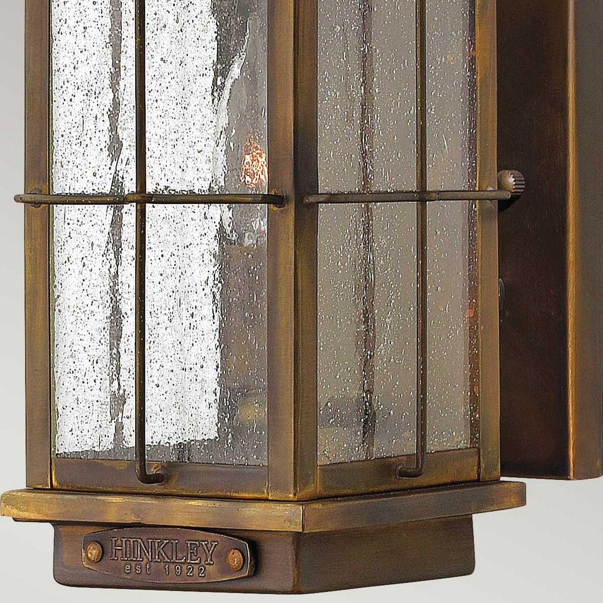 Close-up of the Bingham 1 Light Outdoor Small Wall Lantern, showcasing a vintage-style design with nautical influences. It features a bronze finish and seeded glass panels. A small plaque at the bottom is inscribed with HINKLEY est 1922, giving the lantern its rustic and elegant appearance.
