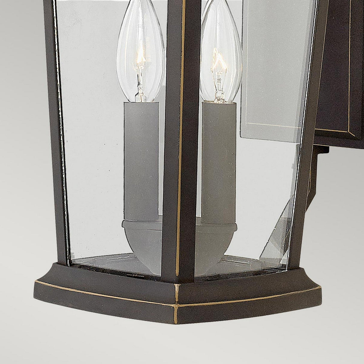 Close-up of the Bromley 2 Light Outdoor Medium Wall Lantern in bronze, showcasing a black metal and glass design with two candle-shaped bulbs inside. The fixture blends traditional design elements with clean lines and beveled edges for a modern aesthetic.