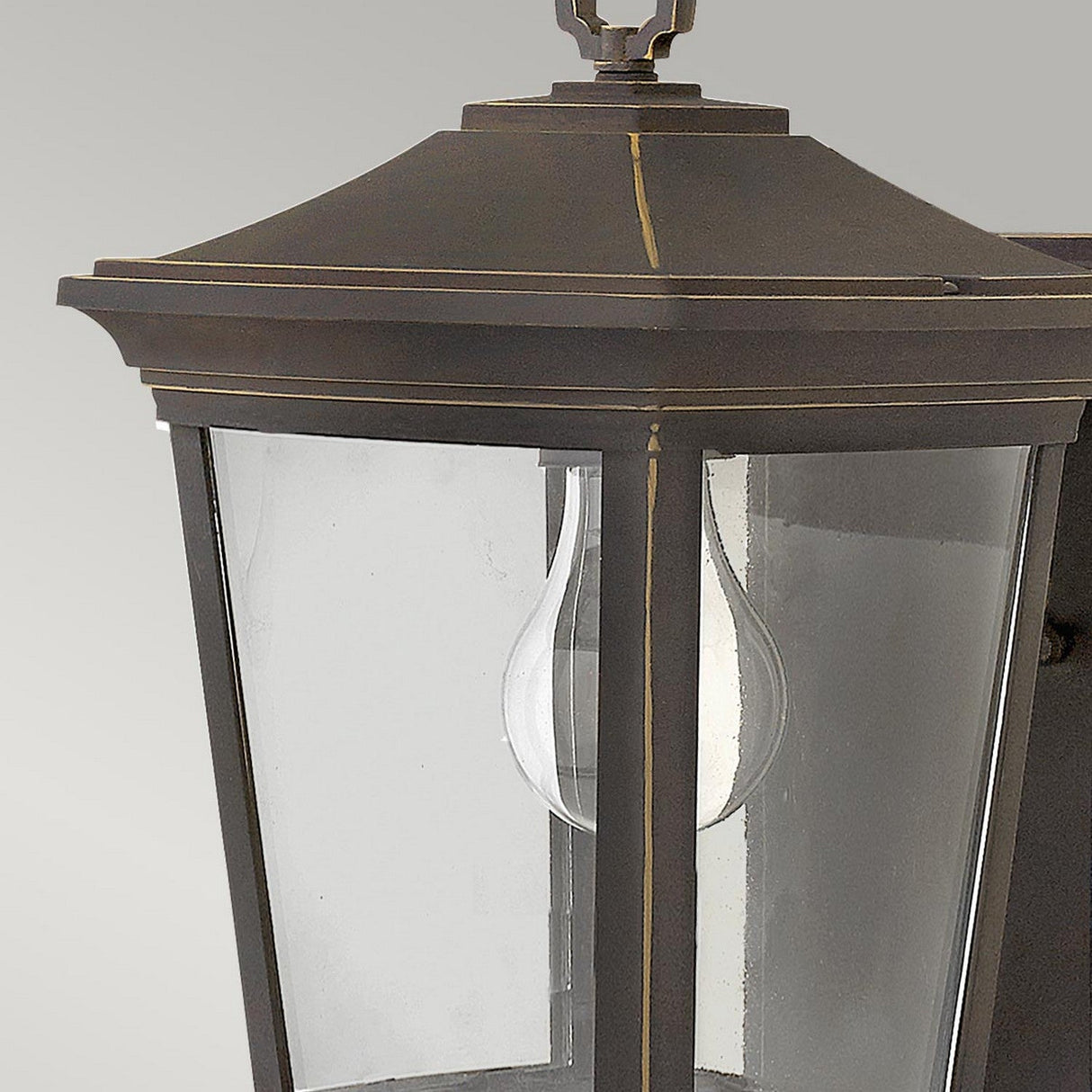 Close-up of the Bromley 1 Light Outdoor Small Wall Lantern, made from die-casted aluminum and featuring a bronze finish with clear glass panels and a visible light bulb. The lantern exhibits a classic design with a square top and decorative trim.