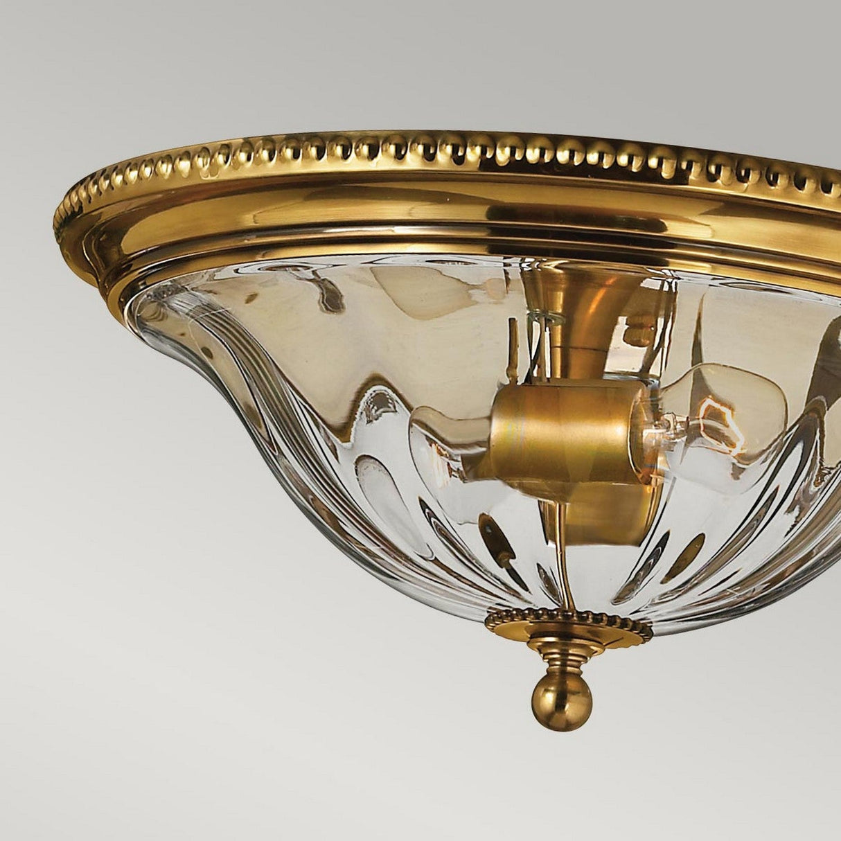 Close-up of the Cambridge 2 Light Flush - Burnished Brass chandelier, showcasing its textured glass dome and intricate gold detailing. The design highlights elegant gold beads around the edge and a central fixture for the lightbulbs, making it an ideal match for New England decor set against a pale gray background.