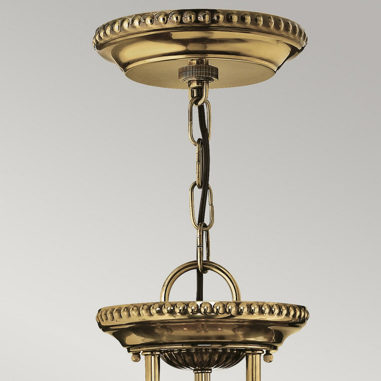 Close-up of a Cambridge 3 Light Small Chandelier in burnished brass, highlighting a decorative chain and intricate New England design. The fixture boasts ornate edges and a reflective surface.