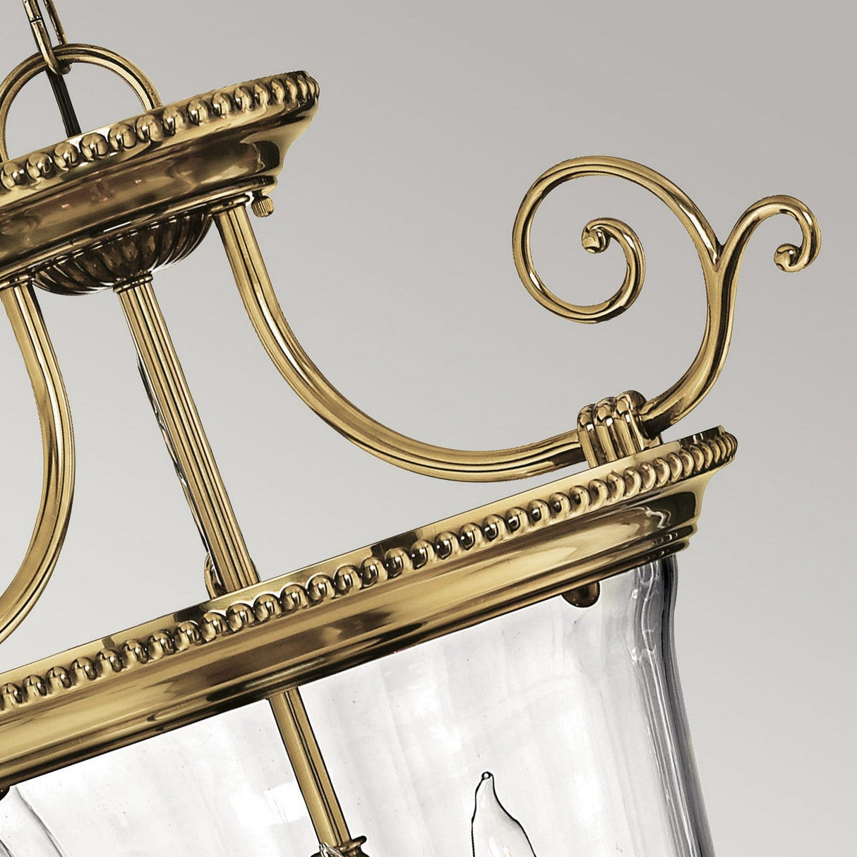 Close-up of a Cambridge 3 Light Small Chandelier, highlighting its ornate scrollwork detailing. This fixture, featuring a burnished brass finish and clear glass elements, embodies the essence of classic New England design with sophistication and timelessness.