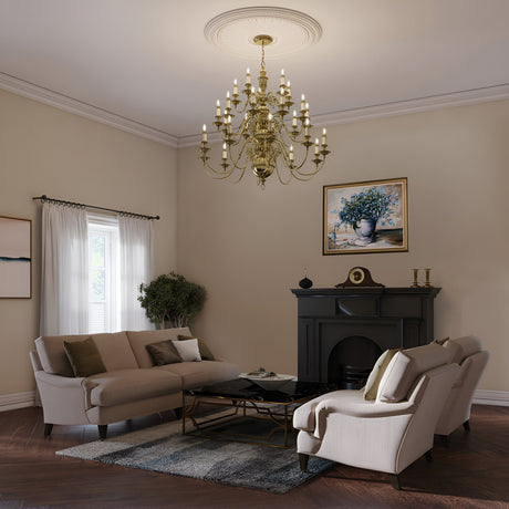 A cozy living room with cream-colored walls features a Cambridge 25 Light Chandelier in Burnished Brass, a fireplace with a clock, two beige armchairs, a gray sofa, and a coffee table. A potted plant and framed artwork add decor. Light filters through a window with sheer curtains, evoking New England elegance.