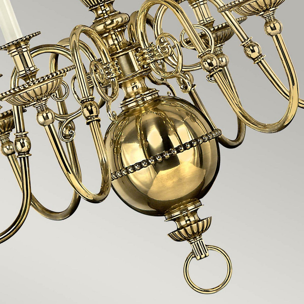 The Cambridge 6 Light Chandelier - Burnished Brass is highlighted in a close-up, revealing its elaborate detailing. Its design includes intricate scrollwork and a central spherical adornment, with optic glass shades that enhance its elegance against a simple gradient background.