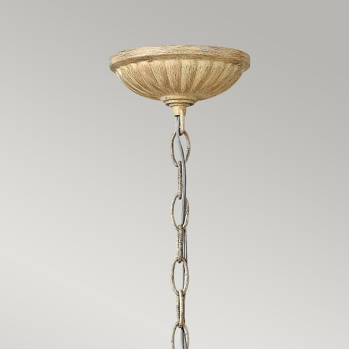The Carabel 1 Light Mini Pendant in Brushed Champagne is suspended by a decorative chain with an antique finish, attached to a ceiling mount featuring a textured, beige canopy. The pendant's pierced metalwork beautifully contrasts against the plain gray background.