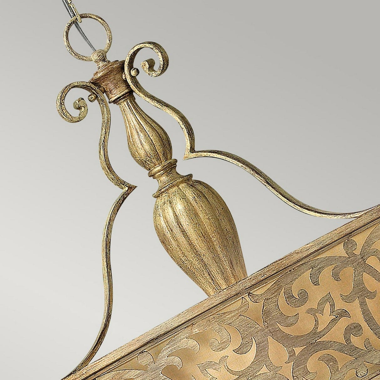 A close-up of an ornate, gold-colored metal hanging pendant light showcases intricate floral patterns and elegant curves, resulting in a vintage and sophisticated appearance similar to the Carabel 3 Light Chandelier - Brushed Champagne, all set against a plain gray background.