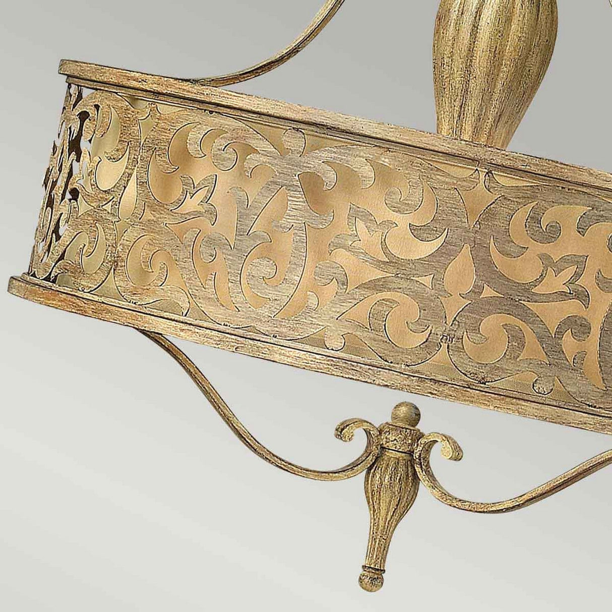 A close-up view showcases an ornate gold metal ring with detailed scrollwork and a decorative finial suspended beneath. The brushed champagne finish enhances the floral and vine motifs, giving it the elegant appearance of the Carabel 3 Light Chandelier - Brushed Champagne against a light background.