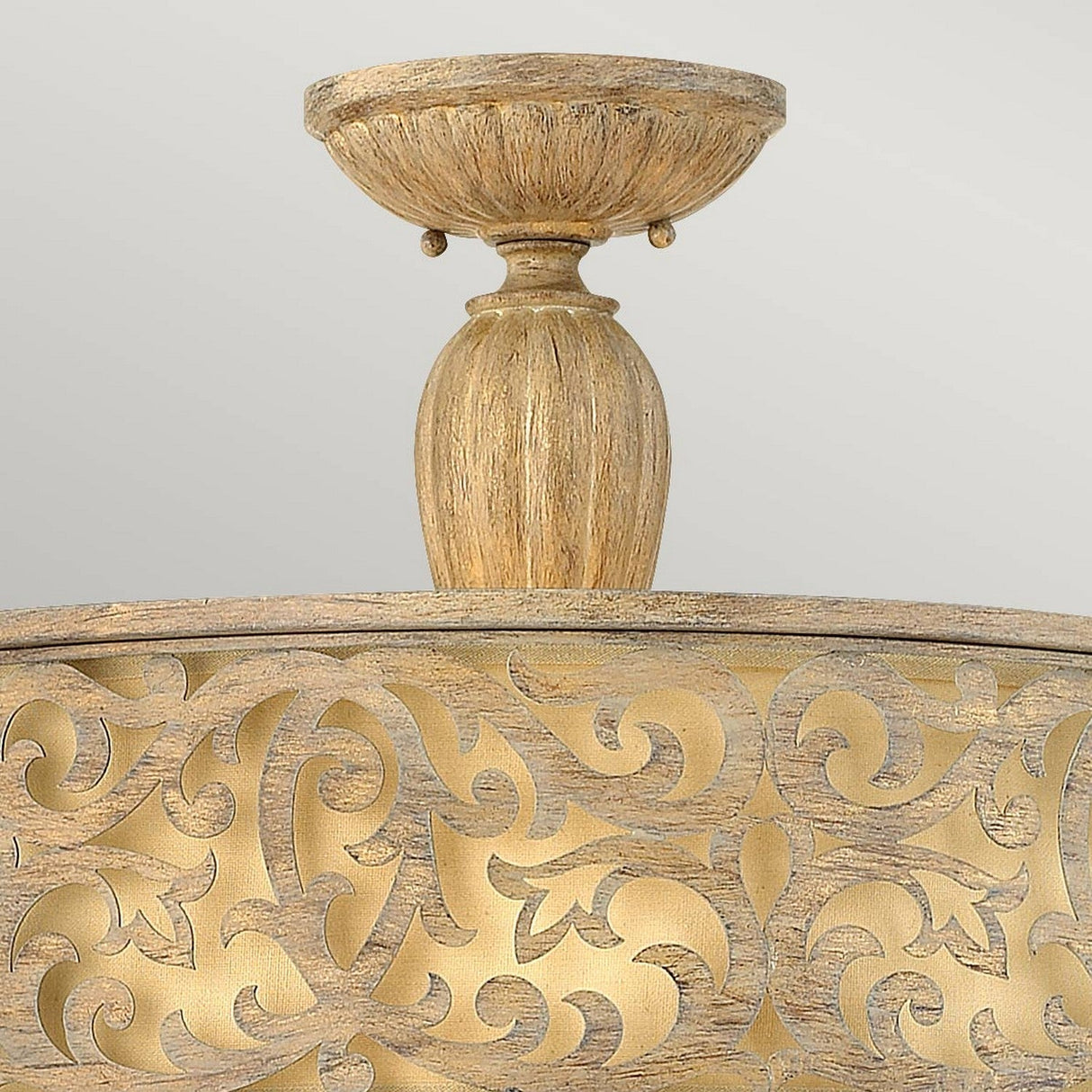 The Carabel 3 Light Large Semi Flush in Brushed Champagne boasts ornate gold and wood-toned details with intricate vine-like patterns and a rounded base. Complemented by ivory linen shades, this lighting fixture shines against a neutral gray background, adding a sophisticated touch to any space.