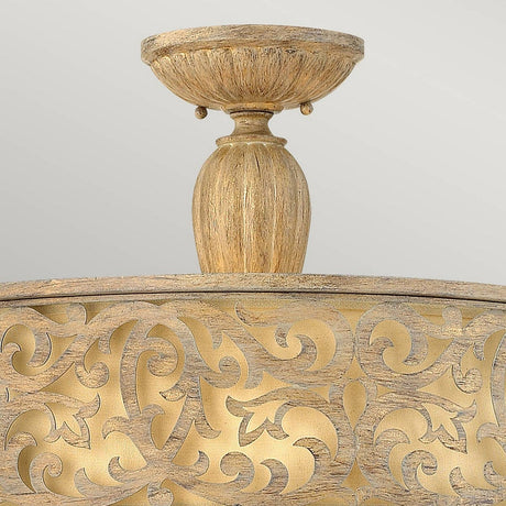 The Carabel 3 Light Large Semi Flush in Brushed Champagne boasts ornate gold and wood-toned details with intricate vine-like patterns and a rounded base. Complemented by ivory linen shades, this lighting fixture shines against a neutral gray background, adding a sophisticated touch to any space.