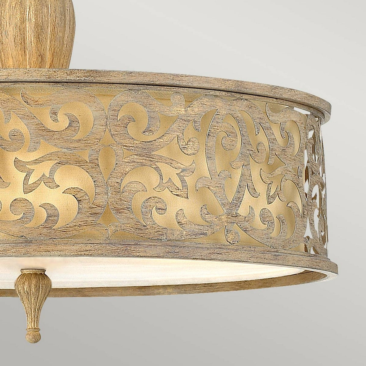 A close-up showcases the Carabel 3 Light Large Semi Flush, highlighting its ornate ceiling light fixture with an intricate, swirling cut-out design on a brushed champagne band. The semi-flush lighting emits a soft glow through the pattern, enhancing its elegant and decorative appearance.