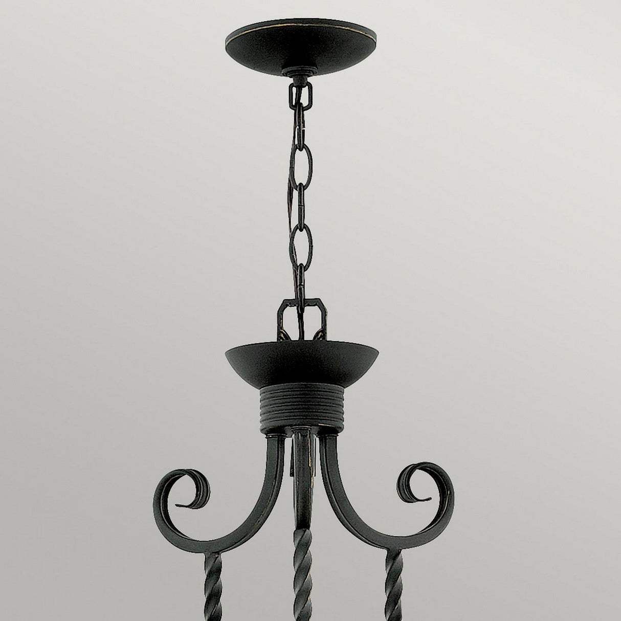 A Casa 5 Light Chandelier - Black hangs from the ceiling by a chain, boasting a wrought iron frame with elegant, curved metalwork and a rustic, dark finish. Its intricate details and timeless charm are highlighted by the plain, light-colored ceiling.