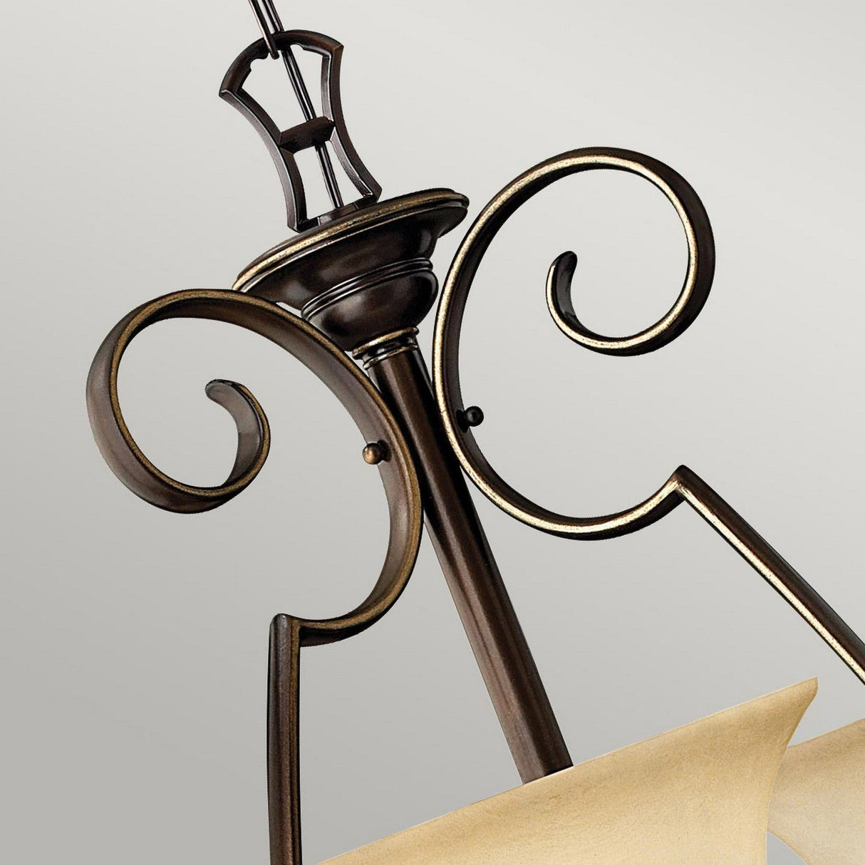 A detailed view of the Cello 9 Light Chandelier in antique bronze highlights its elegant scrollwork. The fixture is complemented by a cream-colored faux alabaster glass shade, adding classic and sophisticated charm against a neutral backdrop.