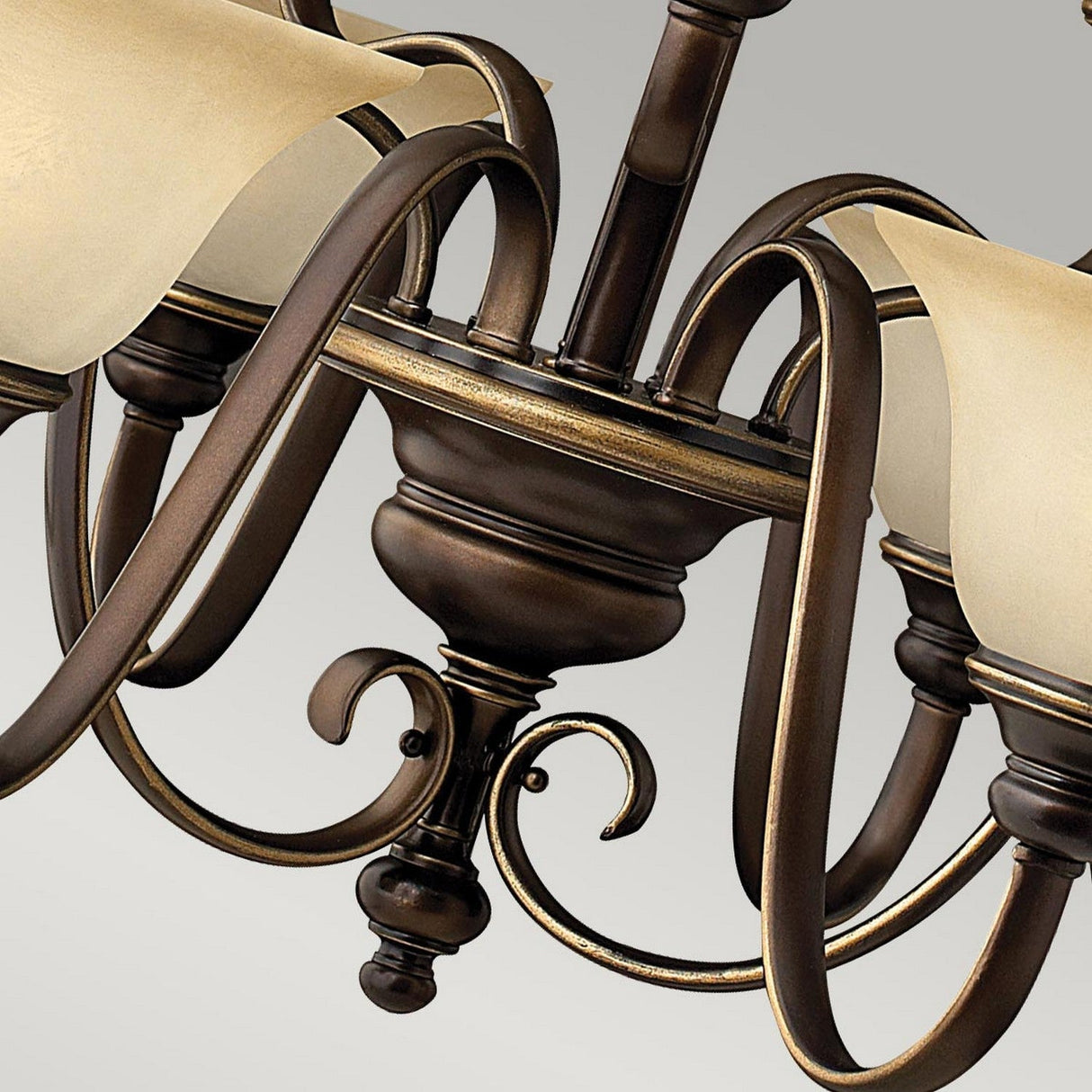 Close-up of the Cello 9 Light Chandelier in Antique Bronze, showcasing its elegant curves and faux alabaster glass light shades. The intricate metalwork features scroll designs, embodying a traditional and sophisticated style.