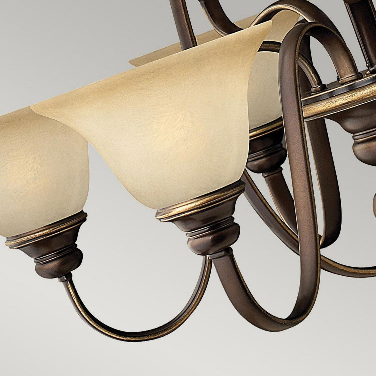 A close-up of the exquisite Cello 9 Light Chandelier - Antique Bronze showcases its elegantly curved metal arms and cream-colored faux alabaster glass shades, all set against a neutral backdrop, with an antique bronze finish that exudes a subtle vintage charm.