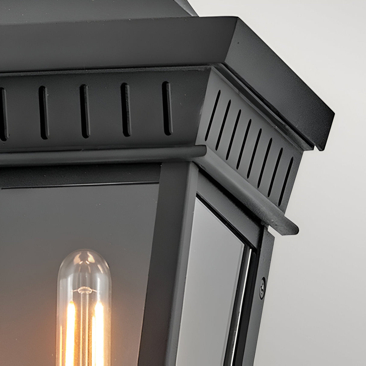Close-up of the Chapel Hill 2 Light Outdoor Half Wall Lantern in black with clear glass panels and glowing bulbs, mounted on a light gray wall.