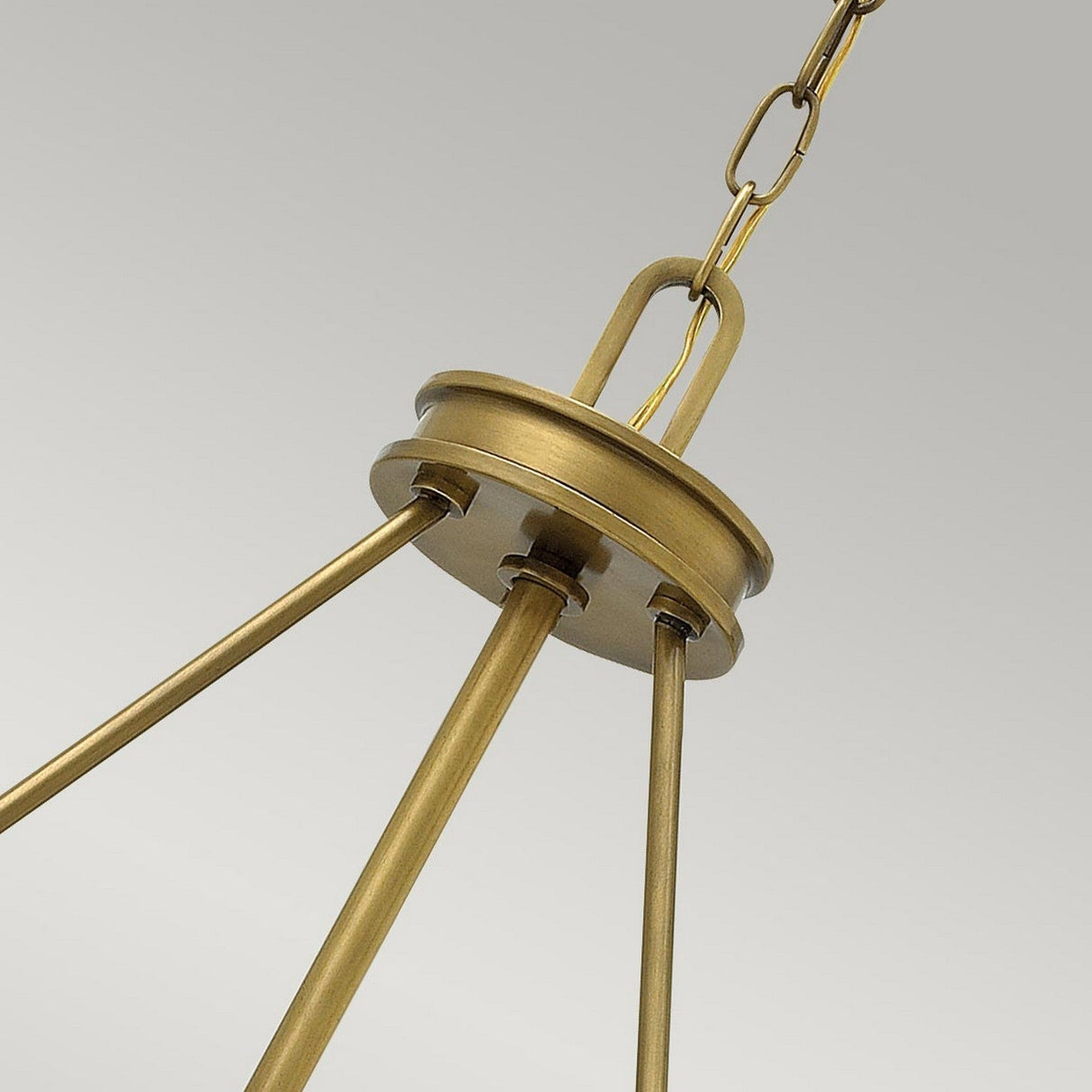 Close-up of the Collier 4 Light Chandelier - Heritage Brass showcasing four rods extending from a circular base, connected by a chain. With its classic Mid-Century Design, this piece elegantly stands out against the soft gray background.
