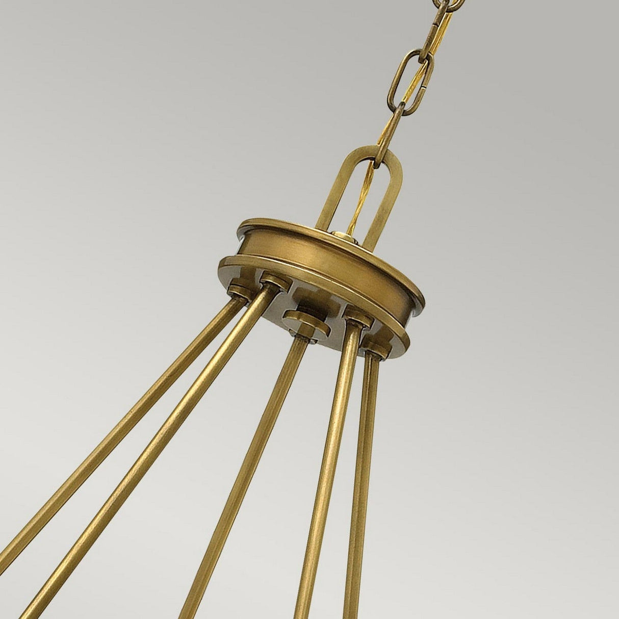 Close-up of the Collier 5 Light Chandelier in Heritage Brass, showcasing a Mid-Century inspired silhouette with chain link attachment and four vertical rods converging at the top. The design is sleek and modern against a plain gray background.