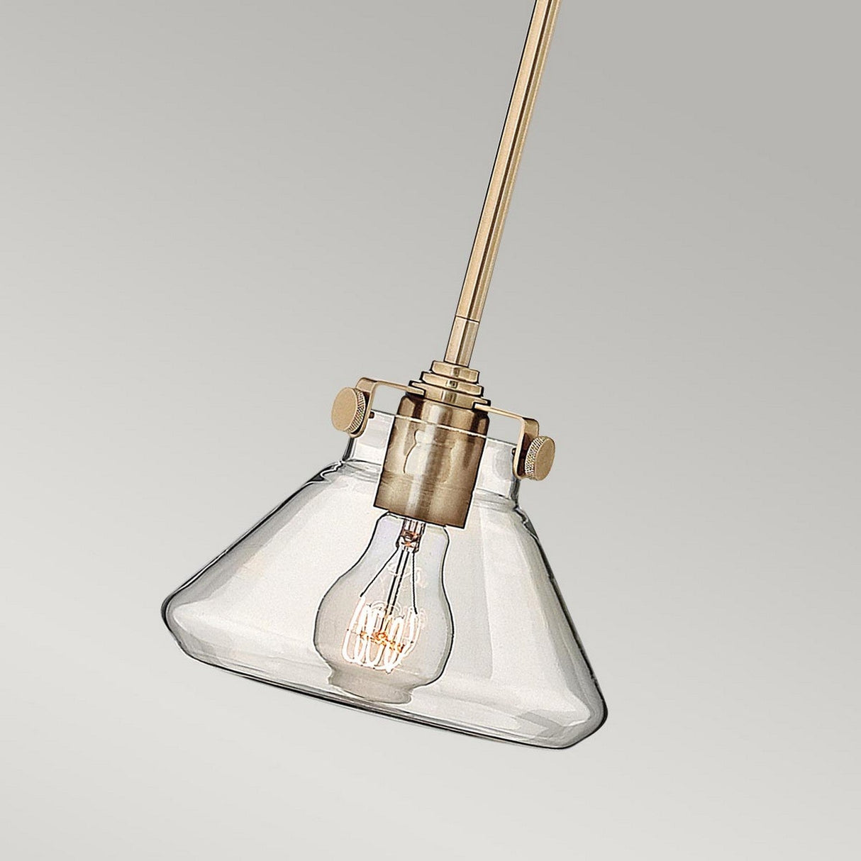The Congress 1 Light Clear Glass Pendant in Brushed Caramel features an exposed vintage-style LED filament lamp, set against a neutral gray background.