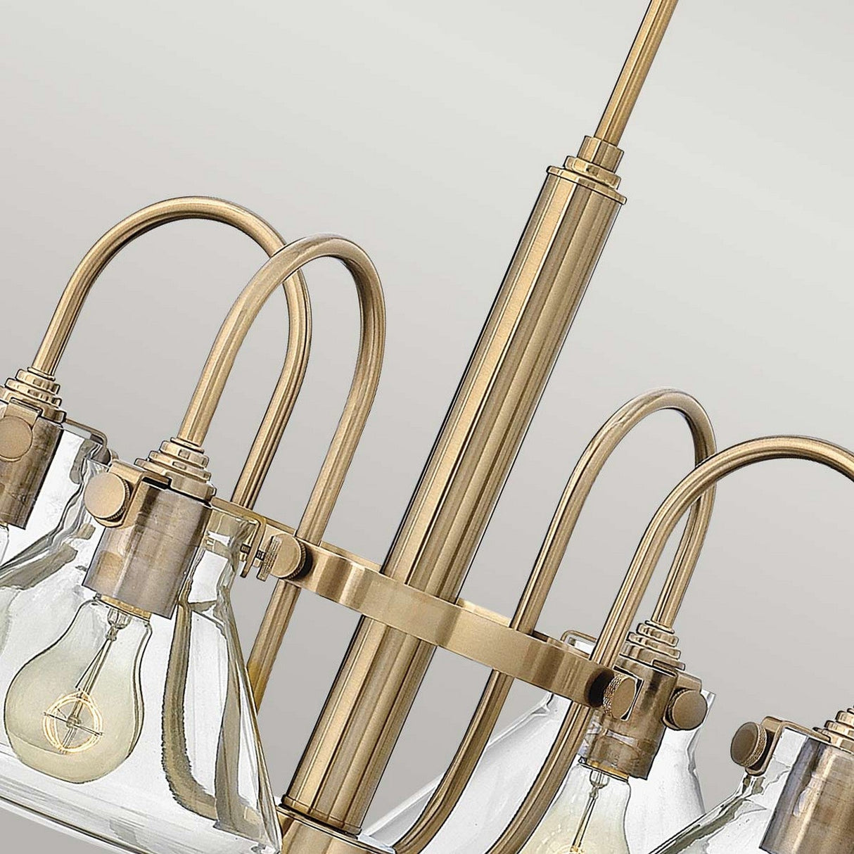 Close-up of the Congress 4 Light Clear Glass Chandelier, featuring exposed light bulbs on a curved metal frame. The design's elegant, vintage accent highlights the craftsmanship of its brass and brushed caramel metalwork, creating a timeless appeal.