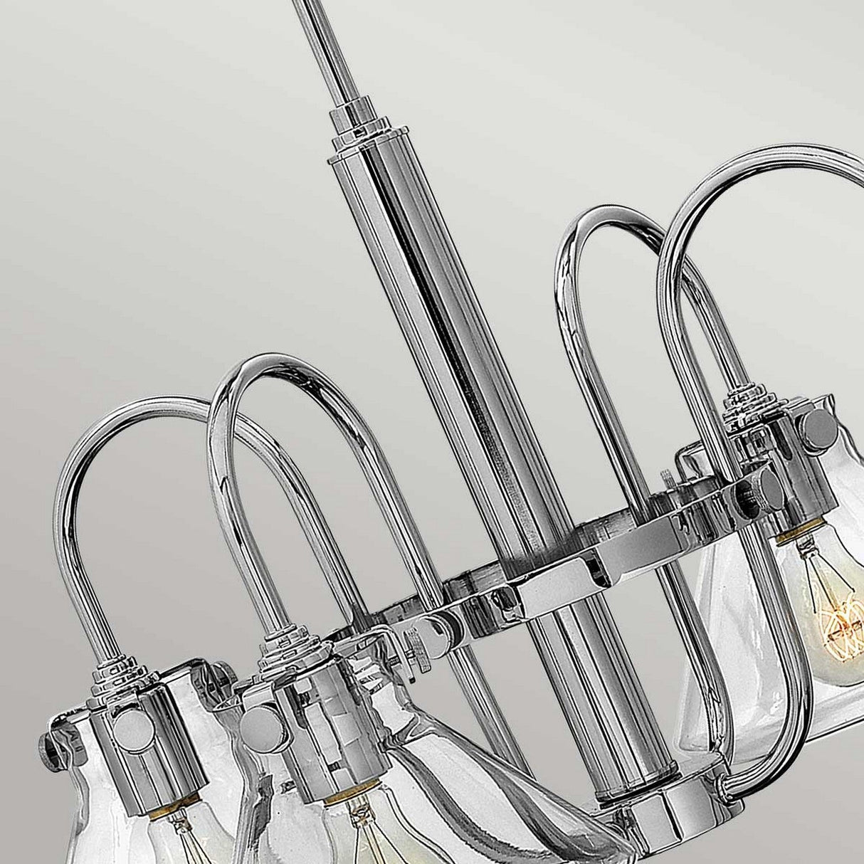 A detailed view of the Congress 4 Light Clear Glass Chandelier - Chrome highlights its several curved metal arms and transparent glass shades, each revealing a visible light bulb, showcasing modern elegance against a light gray backdrop.
