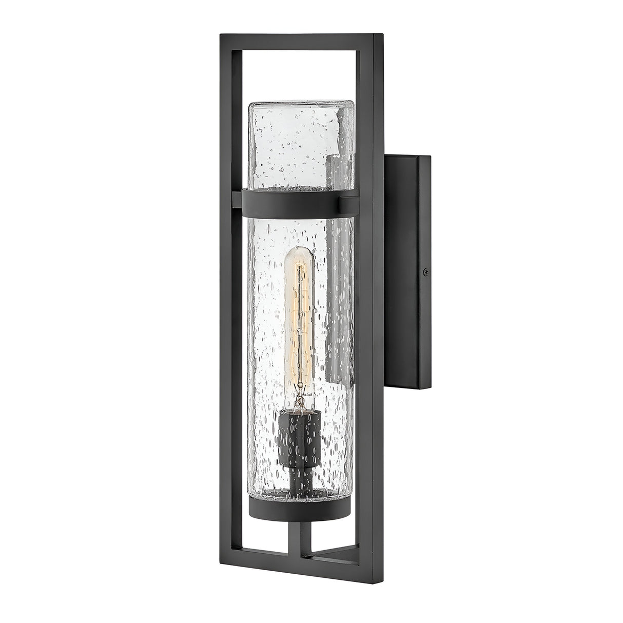 The Cordillera 1 Light Outdoor Wall Light - Black is accentuated by a modern frame, showcasing a rectangular black metal design and a cylindrical glass cover with a textured, bubbled surface. Inside, an exposed vintage-style bulb contributes an industrial flair to this sleek fixture.