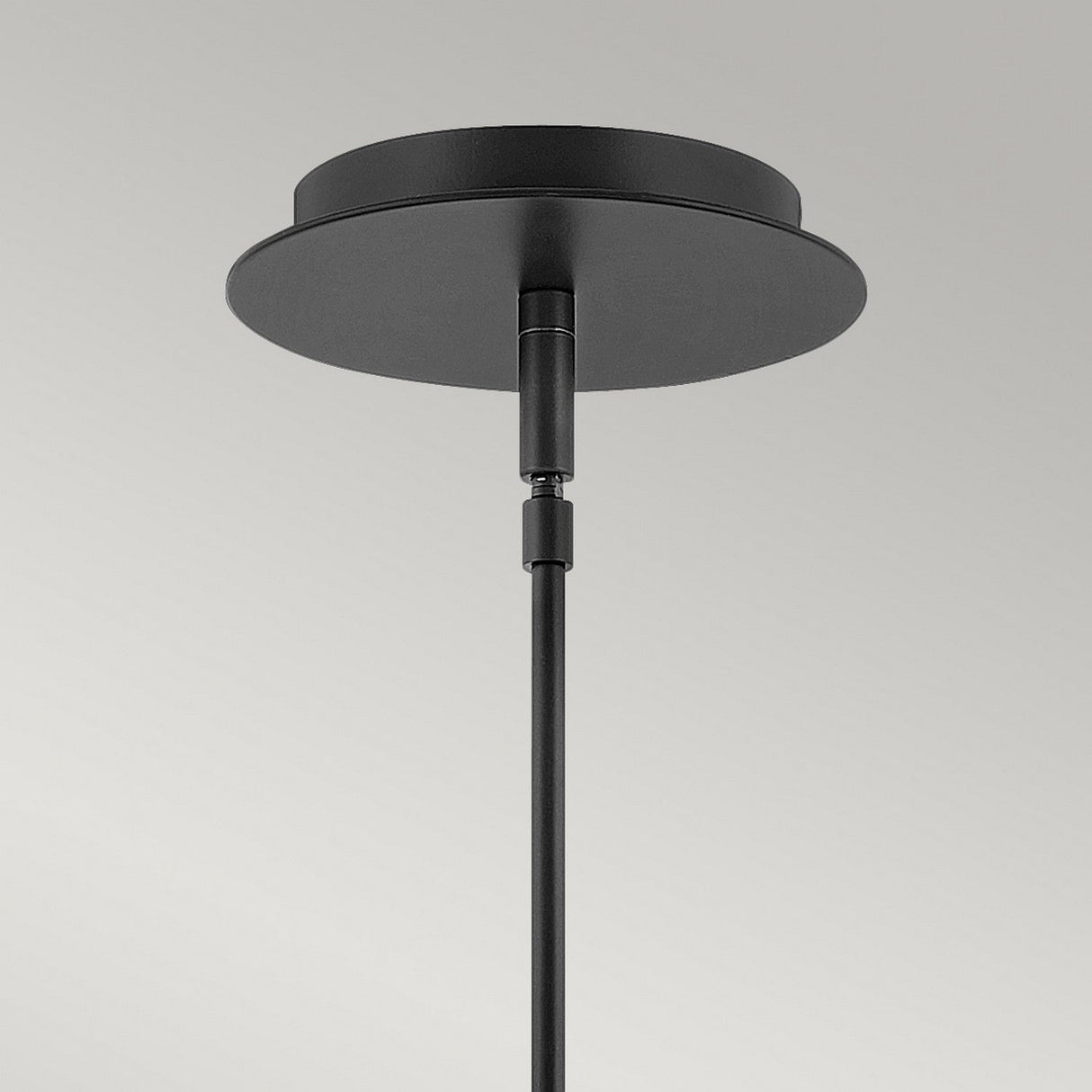 Close-up of the Dax LED Mini Pendant - Black, a modern lighting fixture with a sleek, metallic finish set against a neutral gray background. The black ceiling-mounted rod features a circular base and is vertically attached, providing energy-efficient illumination.