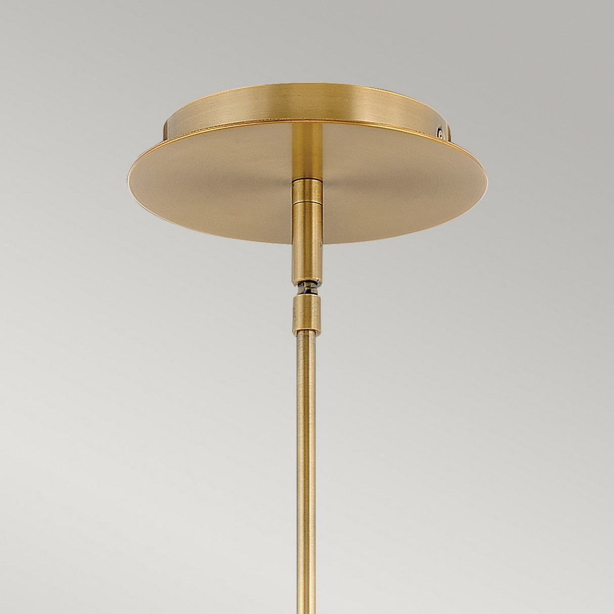 A close-up of the Dax LED Mini Pendant in Heritage Brass, featuring a round ceiling mount and a sleek, straight rod extending downward against a plain gray background, embodies energy-efficient lighting.