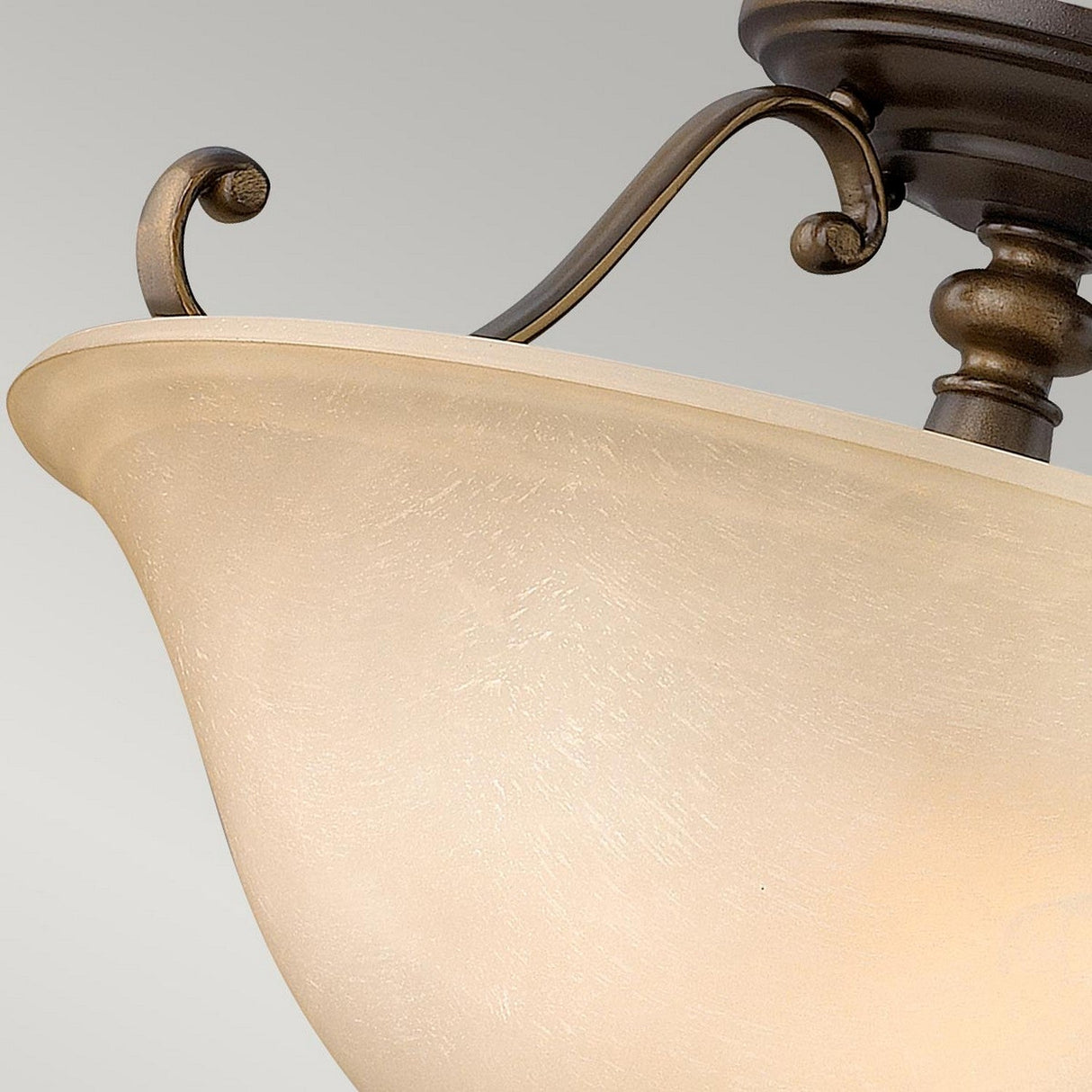A close-up of the Dunhill 2 Light Semi Flush in bronze showcases its vintage-inspired design, featuring ornate metal detailing and a frosted glass shade. The elegantly curved arms and textured shade add a classic touch to the backdrop of a neutral background.