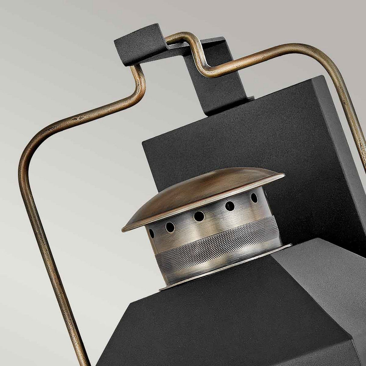 Close-up of a Fitzgerald 3 Light Outdoor Large Wall Lantern in black with burnished bronze accents. This modern piece is crafted from durable aluminum and features a unique perforated design with a handle, set against a gradient gray background.