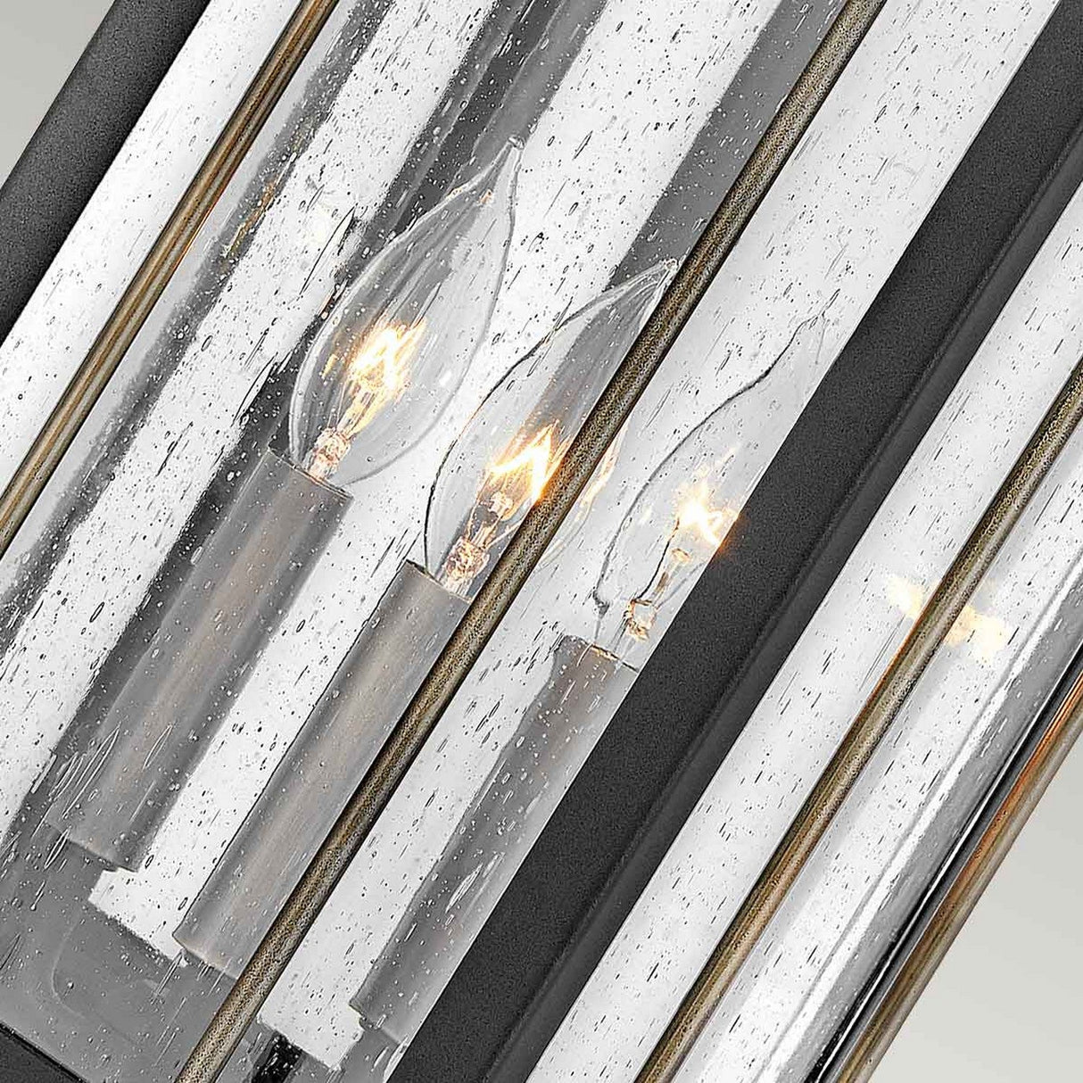 The Fitzgerald 3 Light Outdoor Large Wall Lantern in Black with Burnished Bronze showcases a modern design featuring three candle-style, flame-shaped bulbs encased in glass tubes with a dotted texture. Made from durable aluminum, it provides a reflective effect that enhances the warm glow of its industrial lighting, making it an ideal choice for outdoor wall lantern setups.