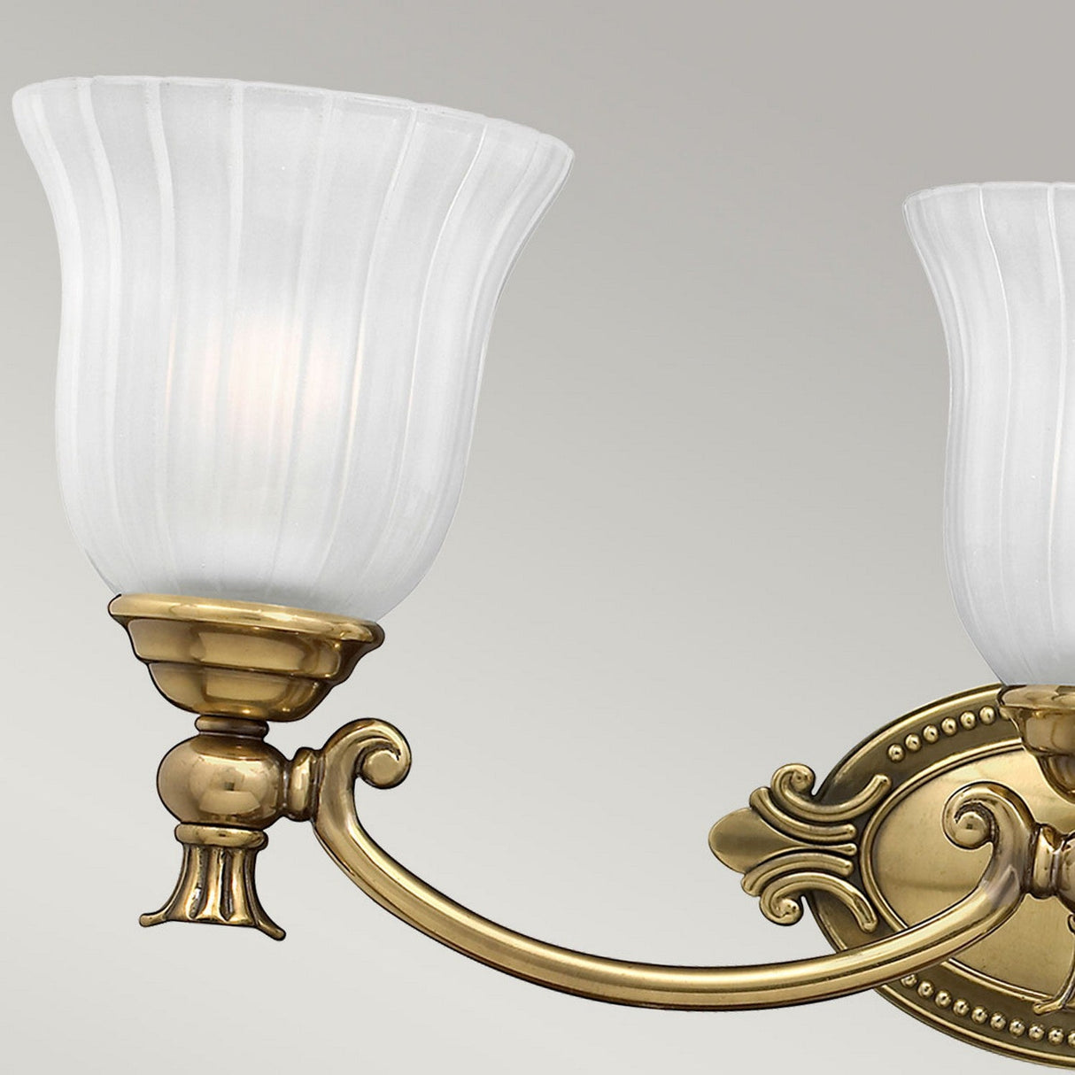 The Francoise 3 Light Wall Light - Burnished Brass showcases a timeless design with frosted ribbed glass shades and an elegant burnished brass fixture. The light is turned off and displayed against a simple light gray background.