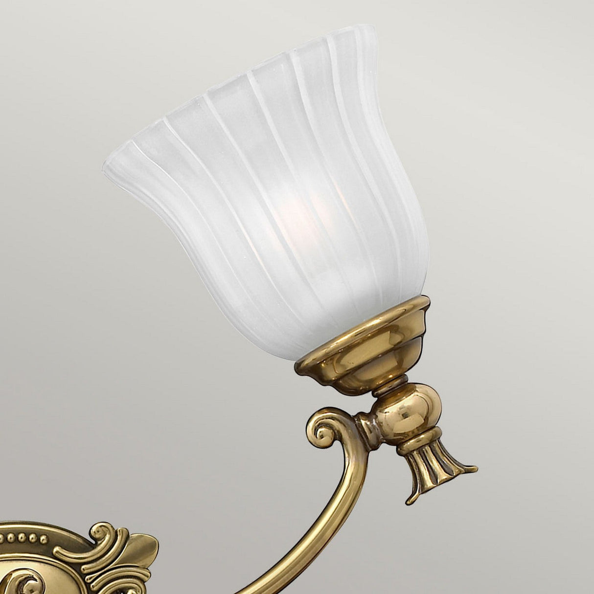 A detailed view of the Francoise 3 Light Wall Light - Burnished Brass showcases its ornate burnished brass base, complemented beautifully by frosted ribbed glass shades that emit a gentle glow against a plain backdrop.
