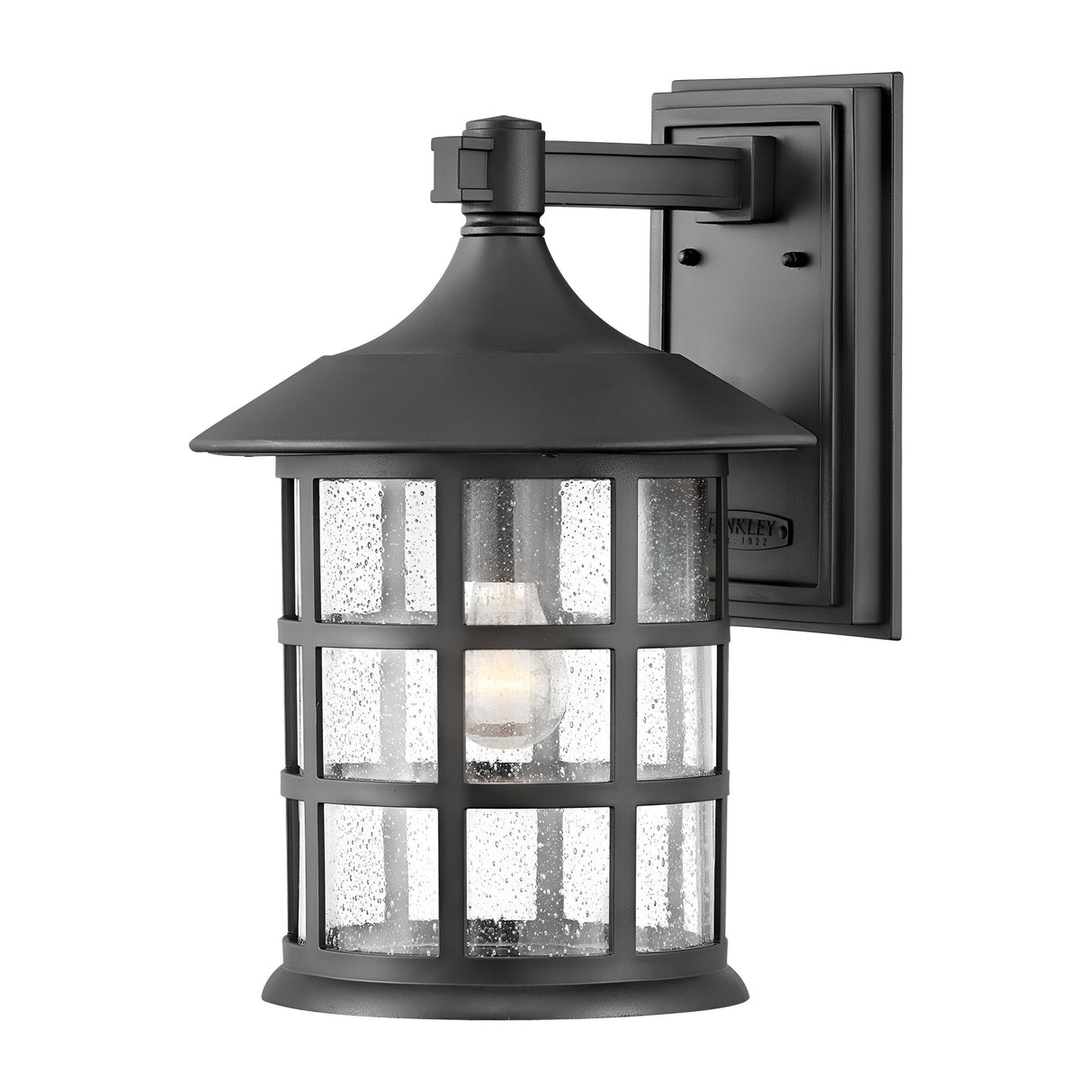 Introducing the Freeport 1 Light Outdoor Large Wall Lantern in black, designed for weather resistance with a classic charm. It features a sleek black finish, a rectangular backplate, and a conical roof. The lantern's clear seeded glass shade envelops a single bulb and is complemented by an enchanting grid-like pattern that adds timeless appeal.