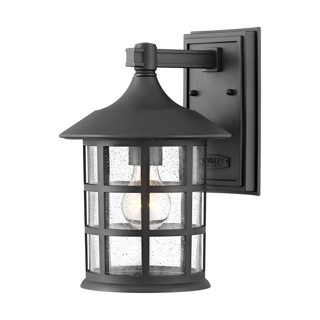 The Freeport 1 Light Outdoor Medium Wall Lantern in black features a grid design with clear glass panels and a lit bulb. This weather-resistant fixture exudes a classic, vintage style and is mounted on a rectangular base.