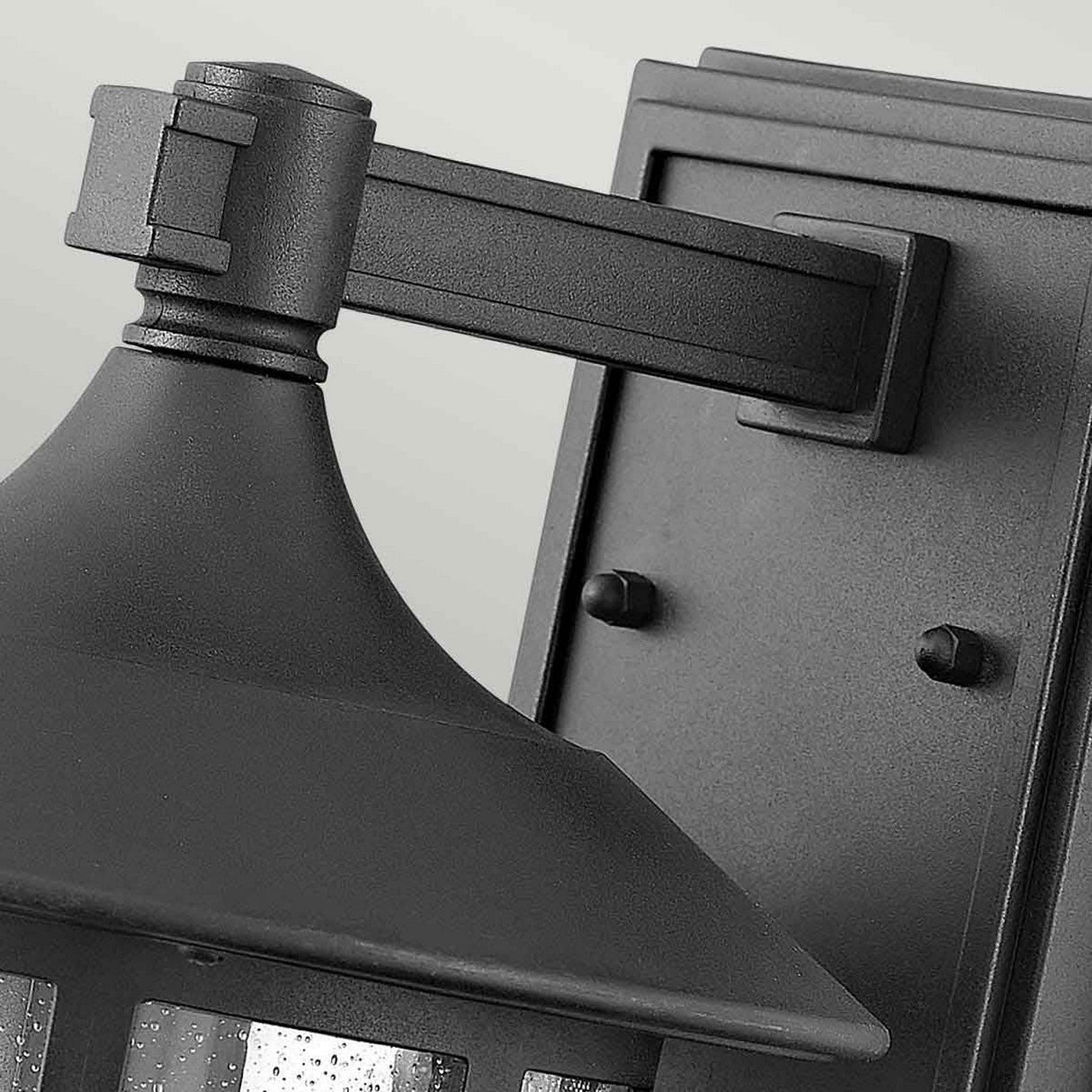Here is a striking close-up of the Freeport 1 Light Outdoor Medium Wall Lantern in a sleek black finish. This durable lantern boasts a rectangular backplate and a triangular top, with textured glass that enhances its elegance, contrasting beautifully against the light background.