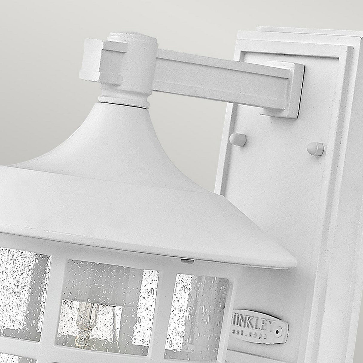 Close-up of the Freeport 1 Light Outdoor Medium Wall Lantern in white. This wall-mounted lantern showcases a clear seeded glass shade with a raindrop texture, designed to withstand the elements. It features a decorative top and is mounted on a rectangular base, making it an ideal choice for outdoor environments.
