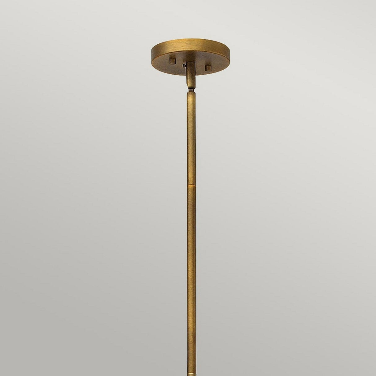 A close-up of the Fulton 13 Light Large Chandelier in bronze and brass, featuring a rod extending downward against a plain gray backdrop. The fixture boasts a minimalistic design with a smooth, metallic finish reminiscent of classic chandeliers.