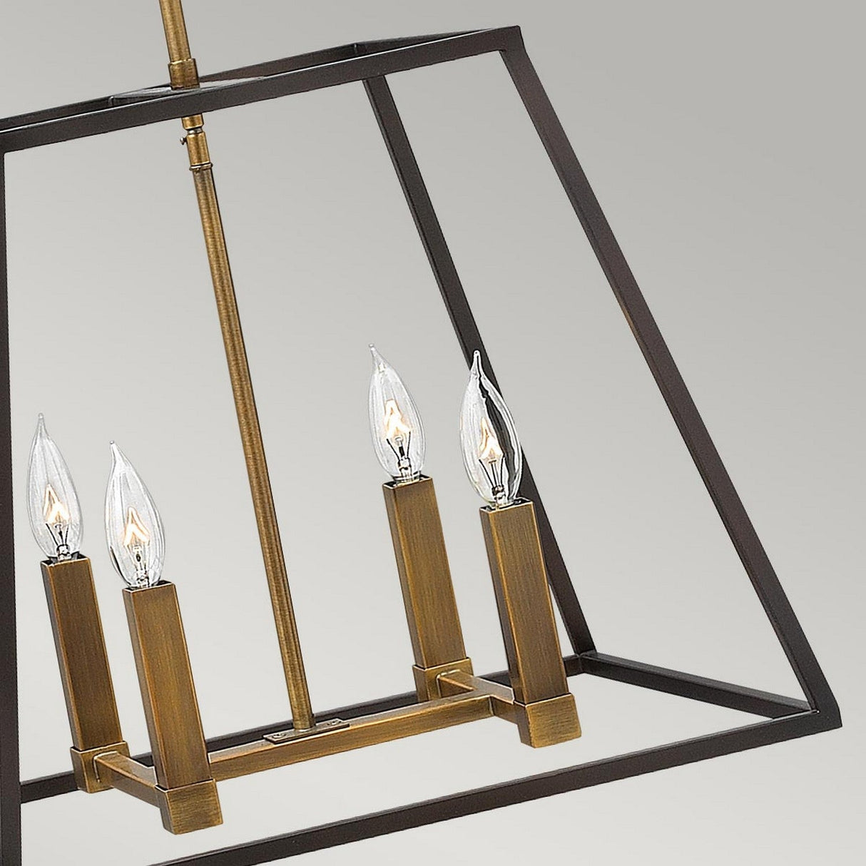 The Fulton 4 Light Pendant Chandelier - Bronze & Brass is a minimalist lighting fixture featuring a geometric frame with a bronze and brass finish. It showcases four upward-facing candle-shaped bulbs arranged within a rectangular structure, set against a gradient gray background.