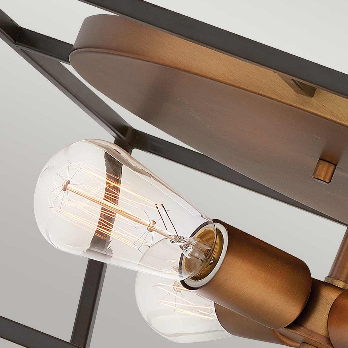 A close-up of a vintage-style bulb with a visible filament in the Fulton 4 Light Flush - Bronze & Brass fixture. This modern geometric ceiling light embodies a sleek, industrial style.