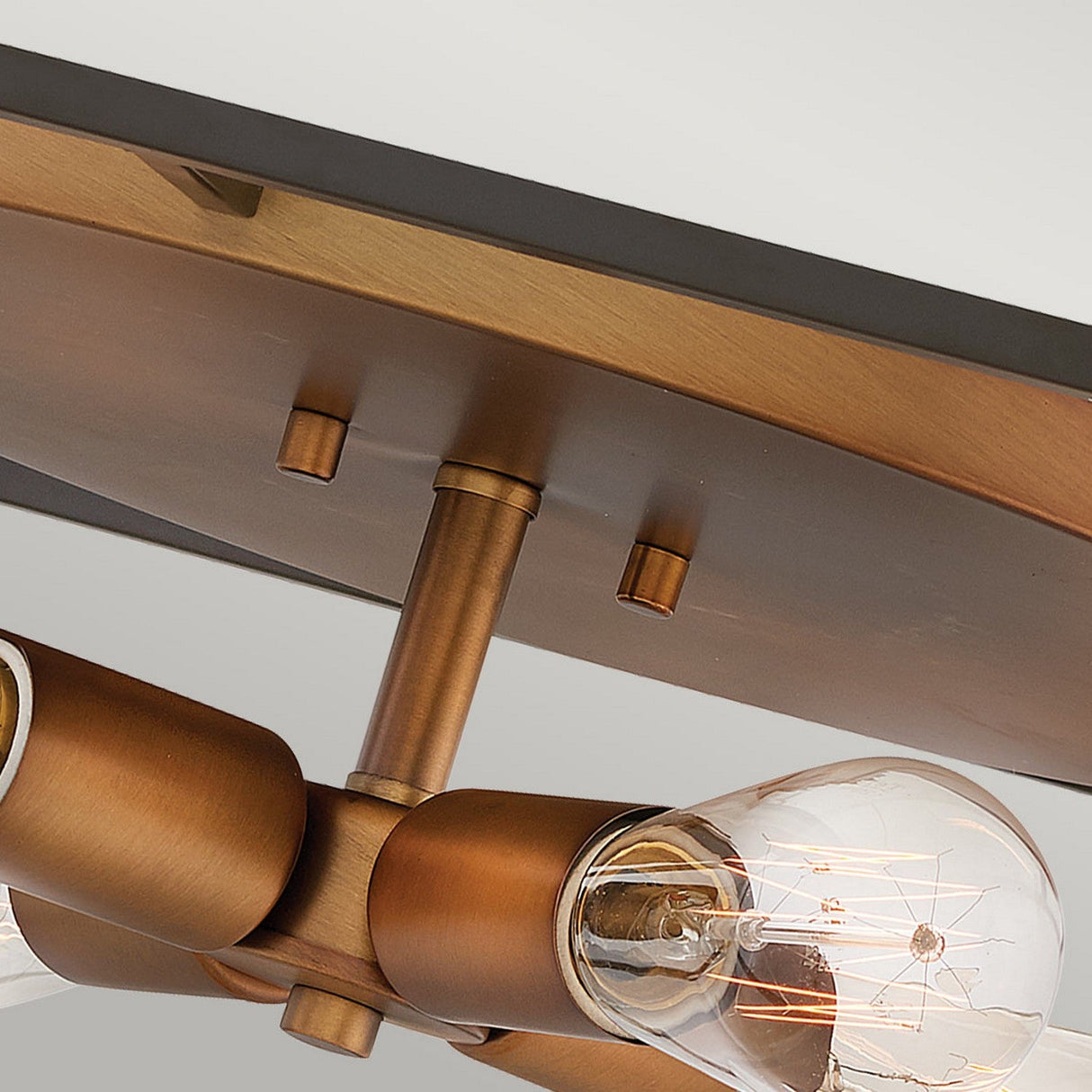 Close-up of the Fulton 4 Light Flush in a bronze and brass finish featuring four exposed Edison bulbs. The fixture boasts a sleek design, mounted on a rectangular base, which enhances its contemporary industrial aesthetic.