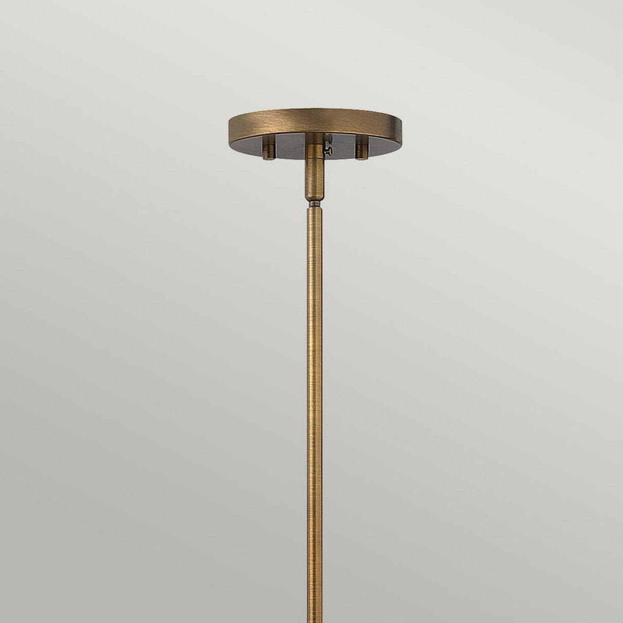 The Fulton 1 Light Pendant, crafted in a combination of bronze and brass, features a minimalist design with a circular base and slender rod against a plain gray background. It embodies modern elegance infused with vintage industrial style, providing an understated yet striking addition to interior spaces.