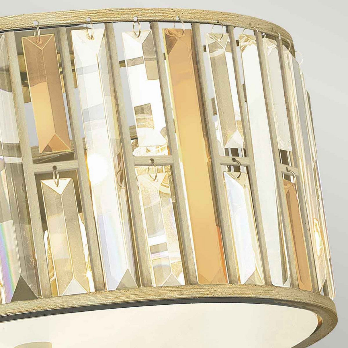 Close-up of the Gemma 3 Light Flush - Gold, a decorative fixture featuring a circular band with vertically arranged translucent and golden panels. These panels reflect light beautifully alongside crystal prisms, creating a warm and elegant ambiance.