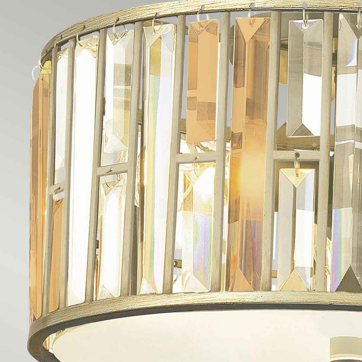A close-up of the Gemma 3 Light Flush - Gold chandelier reveals vertical crystal prisms that beautifully reflect light in shades of gold and silver, while its metallic gold frame enhances its elegant and luxurious appearance.